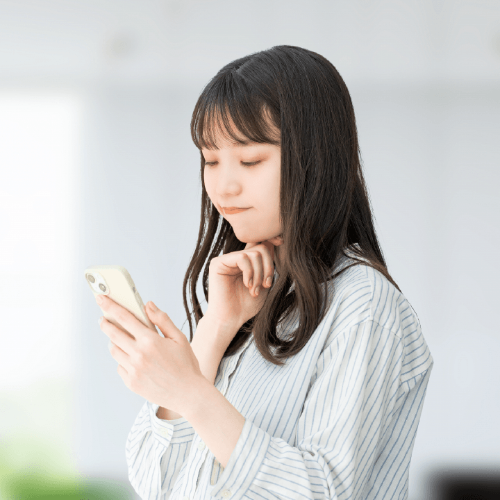 スマホの操作をしながら考えている女性